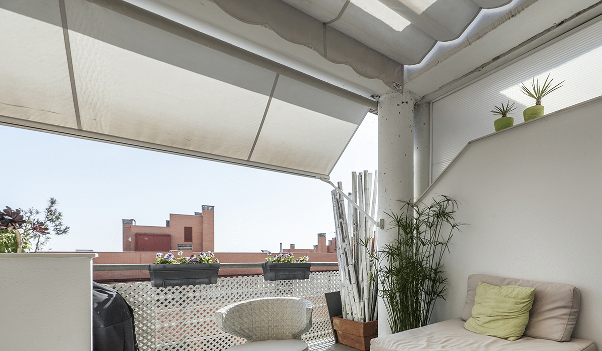 Terraza moderna con plantas y muebles cómodos al aire libre con toldos blancos en las ventanas